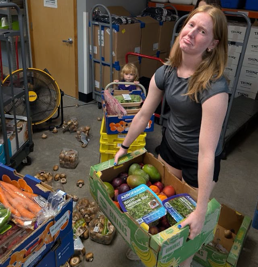 Volunteer carrying a large box of fresh produce in the current warehouse
